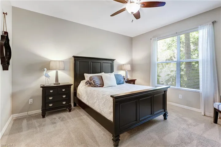 The bedroom features light-colored walls and carpet, a window with blinds and sheer curtains, and a ceiling fan