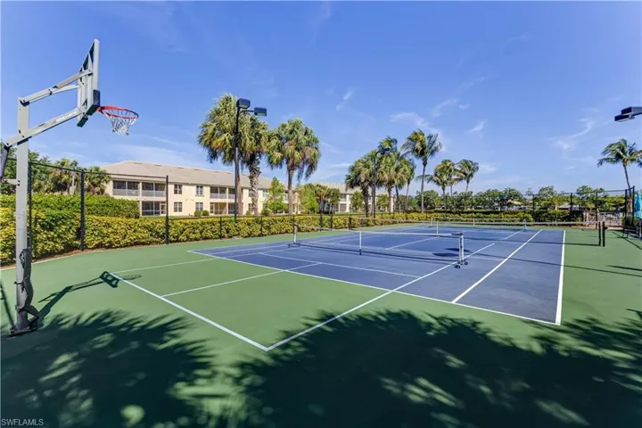 The property offers a vibrant recreational area featuring a tennis court with a basketball hoop, surrounded by lush landscaping and palm trees