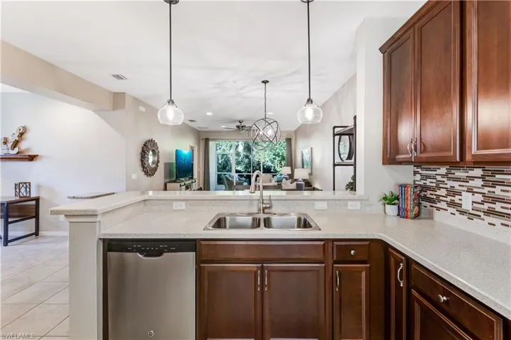 The kitchen features dark wood cabinetry, a stainless steel dishwasher, a double basin sink, and a tiled backsplash