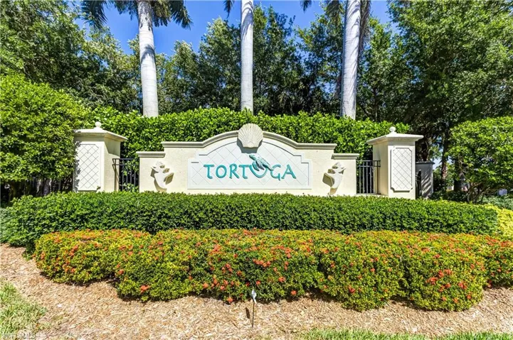 The community entrance features lush landscaping, including trimmed hedges and mature trees, with a decorative sign showcasing the community name