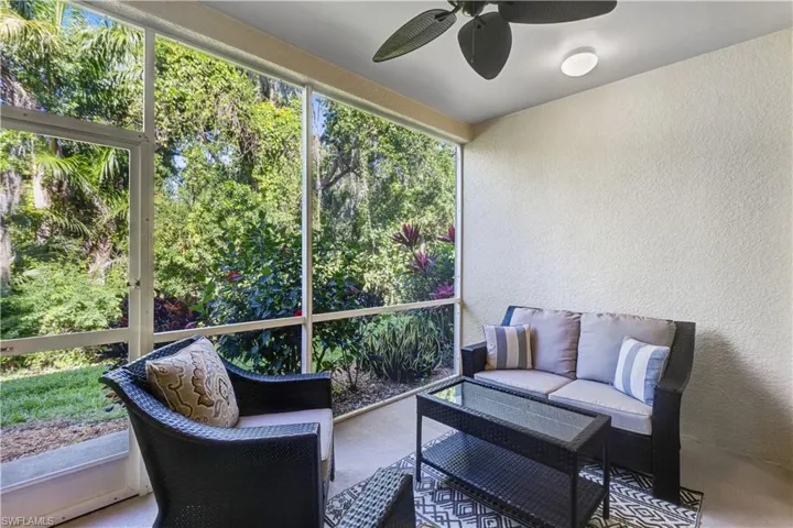 This screened patio offers an outdoor space with views of lush greenery, a textured exterior wall, and a ceiling fan with integrated lighting
