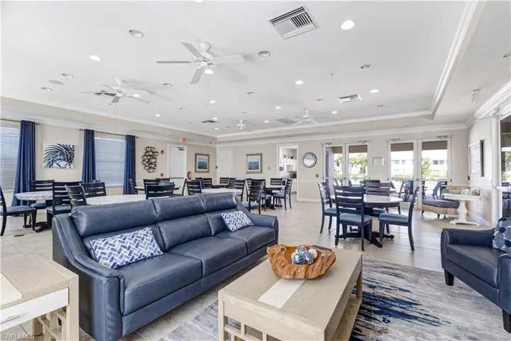 This room features recessed lighting, ceiling fans, and a combination of seating arrangements including a blue sofa and dining tables with chairs