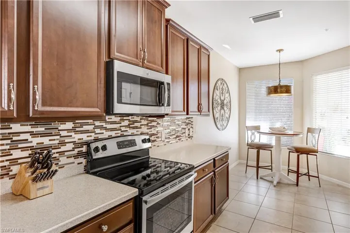 The kitchen features wooden cabinetry, stainless steel appliances, a mosaic tile backsplash, and light-colored countertops