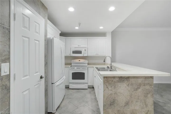 Kitchen featuring sink, white appliances, white cabinetry, ornamental molding, and kitchen peninsula
