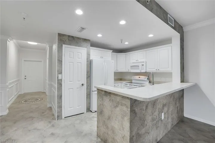 Kitchen with white cabinetry, white appliances, ornamental molding, and kitchen peninsula