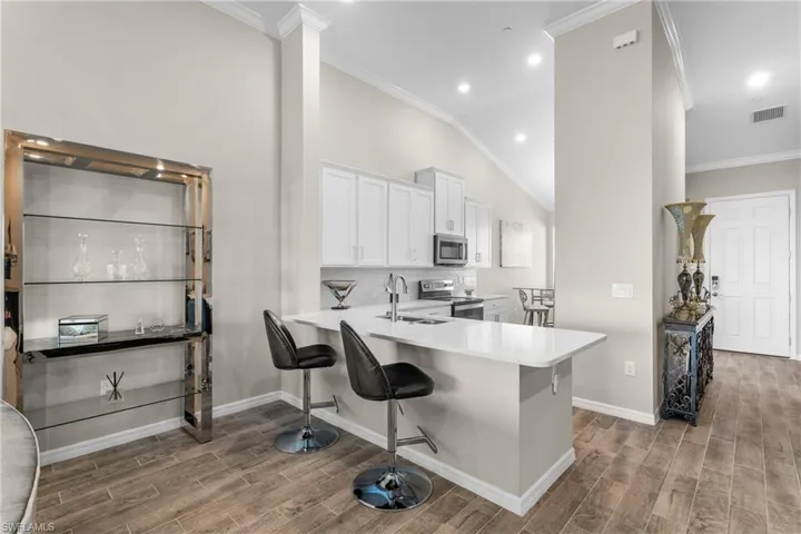 Kitchen with crown molding, a breakfast bar, white cabinetry, tasteful backsplash, and appliances with stainless steel finishes
