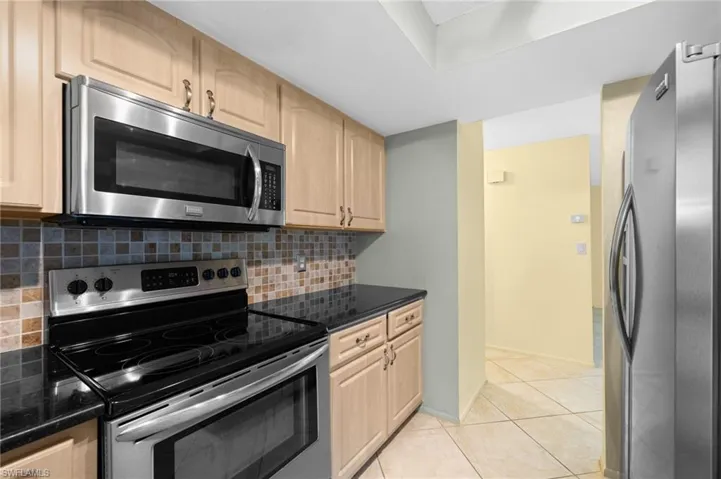 Kitchen featuring dark stone countertops, light tile flooring, tasteful backsplash, and appliances with stainless steel finishes