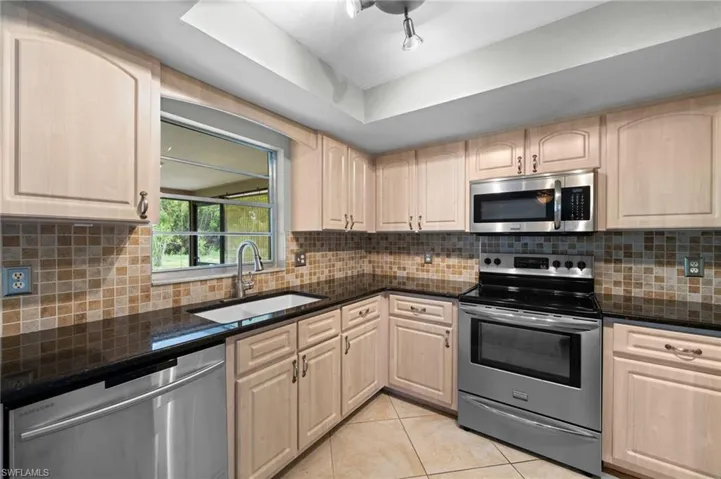 Kitchen with stainless steel appliances, sink, tasteful backsplash, light tile floors, and light brown cabinets