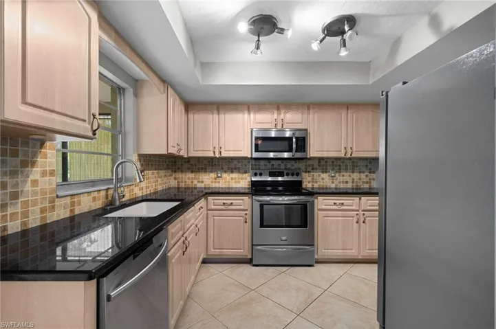 Kitchen with light brown cabinets, tasteful backsplash, stainless steel appliances, a raised ceiling, and sink