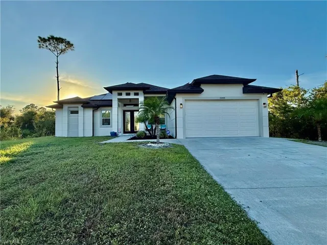 Prairie-style home featuring roof mounted solar panels, a lawn, driveway, an attached garage, and stucco siding