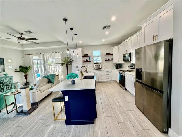 Kitchen with appliances with stainless steel finishes, open shelves, white cabinets, hanging light fixtures, and open floor plan