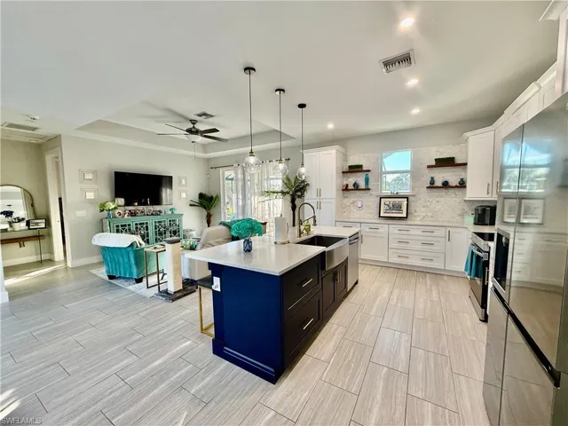 Kitchen with a raised ceiling, white cabinets, stainless steel appliances, hanging light fixtures, and recessed lighting