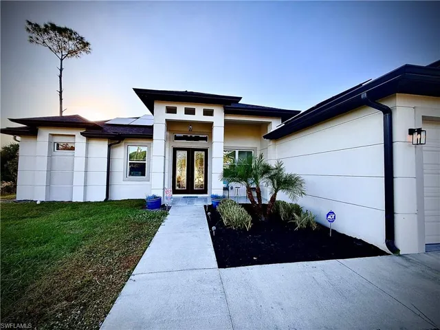 View of front of home with roof mounted solar panels, a yard, stucco siding, and double doors
