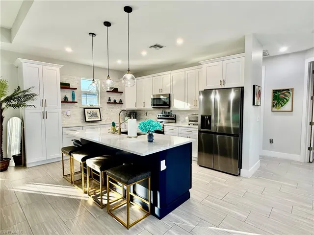 Kitchen with stainless steel appliances, white cabinets, open shelves, decorative light fixtures, and recessed lighting