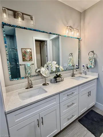 Full bath with double vanity, gray wood-style tile floors, and a shower