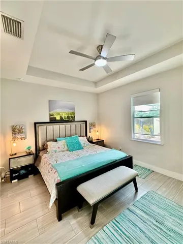 Bedroom with a tray ceiling, wood finish floors, and a ceiling fan