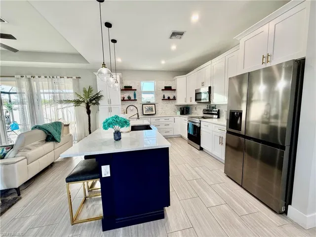 Kitchen with stainless steel appliances, white cabinets, open floor plan, decorative light fixtures, and light stone countertops