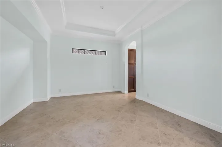 Dining room with arched walkways, a raised ceiling, crown molding, and light tile patterned floors