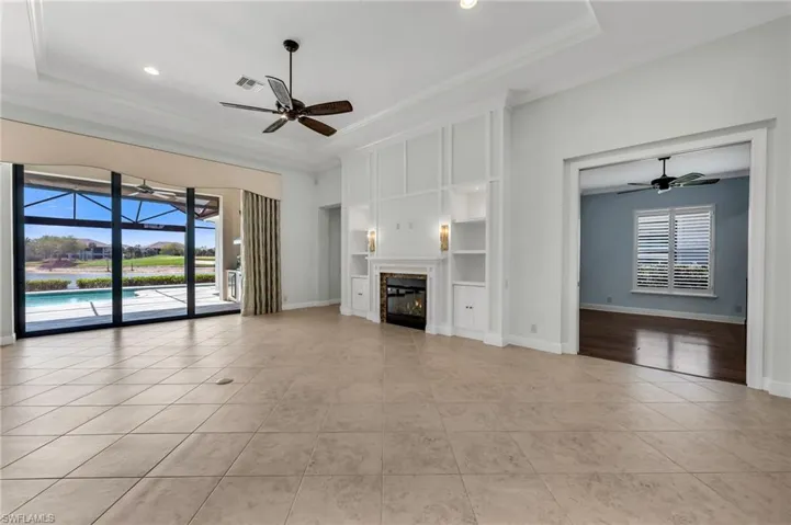 Unfurnished living room with ceiling fan, a sunroom, a glass covered fireplace, built in shelves, and light tile patterned flooring