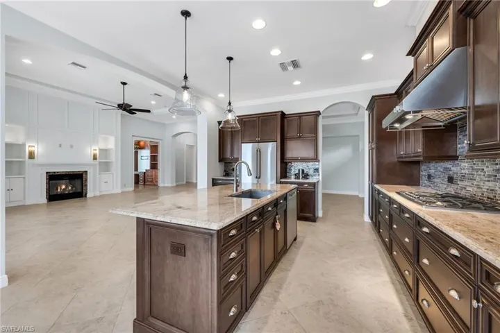 Kitchen with arched walkways, light stone counters, built in shelves, dark wood finish cabinetry, and open floor plan