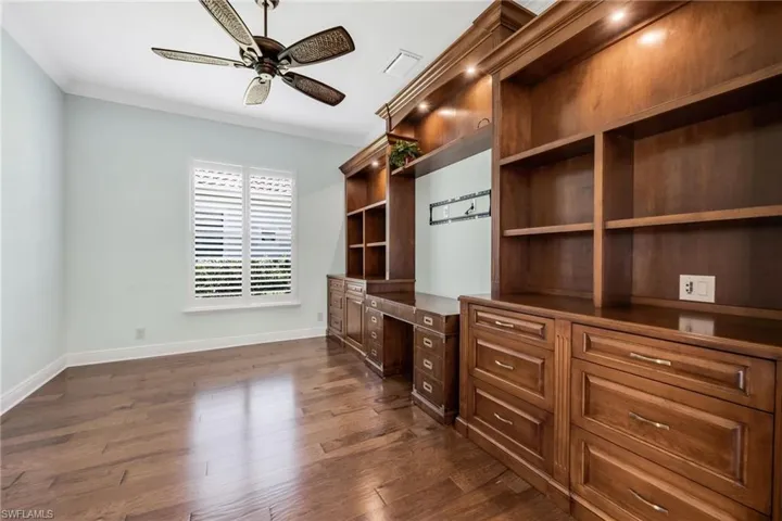 Unfurnished office with built in study area, crown molding, ceiling fan, and dark wood finished floors