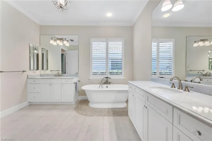 Bathroom with two vanities, ornamental molding, a chandelier, and a freestanding tub