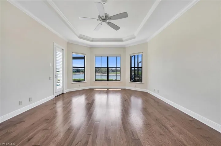 Spare room featuring dark wood-type flooring, a ceiling fan, a tray ceiling, and crown molding