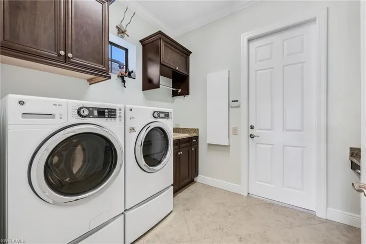 Laundry area with ornamental molding, cabinet space, washer and dryer, and light tile patterned flooring