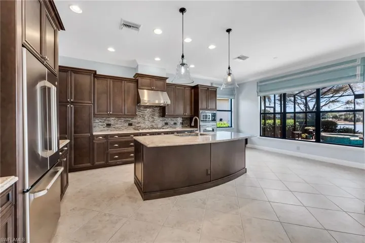 Kitchen featuring stainless steel appliances, a kitchen island with sink, light stone counters, pendant lighting, and light tile patterned floors