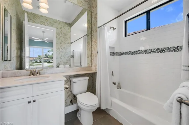 Full bathroom featuring wallpapered walls, plenty of natural light, vanity, shower / bath combo with shower curtain, and dark tile patterned flooring