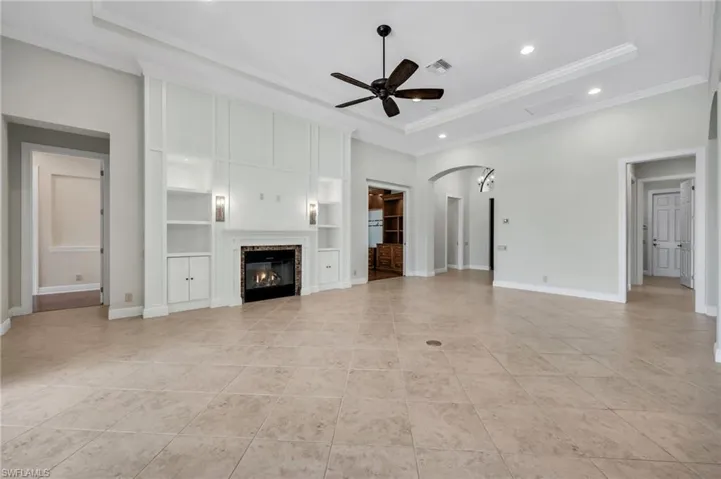 Unfurnished living room with arched walkways, a ceiling fan, a glass covered fireplace, a raised ceiling, and recessed lighting