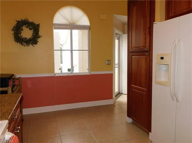 Kitchen featuring white refrigerator with ice dispenser, brown cabinetry, and light tile patterned floors