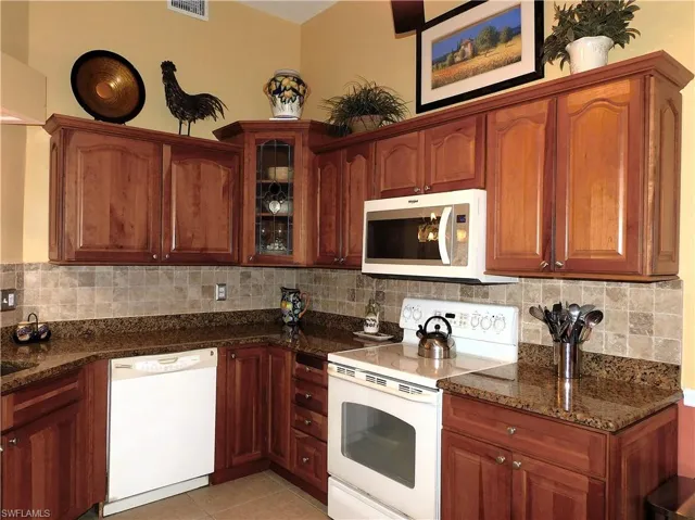 Kitchen with white appliances, dark stone countertops, glass insert cabinets, backsplash, and light tile patterned floors
