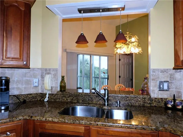 Kitchen with tasteful backsplash, dark stone counters, decorative light fixtures, and brown cabinetry