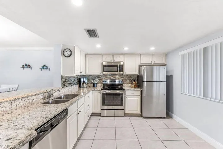 Kitchen with tile backsplash, sink, light colored granite countertops, light tile patterned flooring, and stainless steel appliances