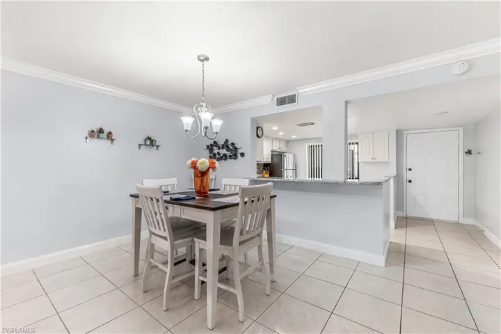 Tiled dining space featuring crown molding and a chandelier and countertop area for bar stools