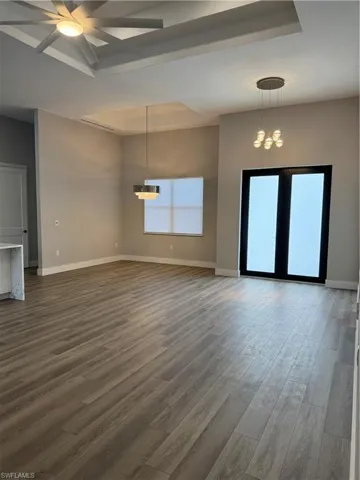 Unfurnished living room featuring ceiling fan with notable chandelier, dark hardwood / wood-style flooring, and a tray ceiling