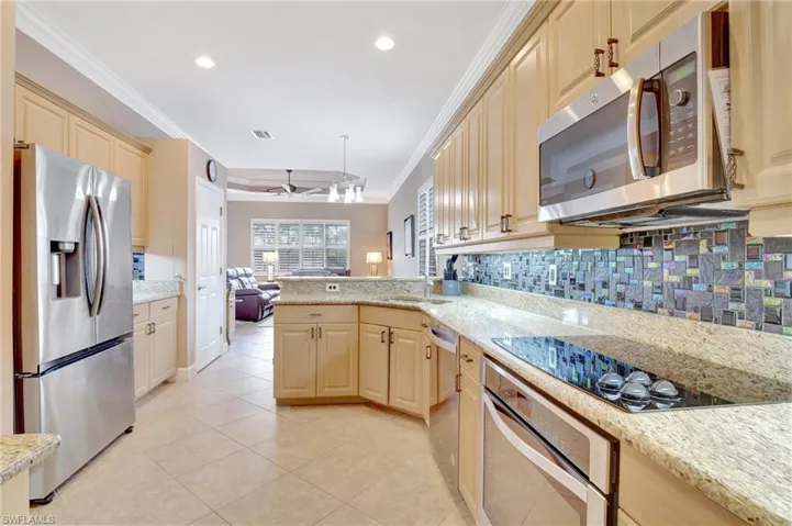 Kitchen with open floor plan, appliances with stainless steel finishes, ceiling fan, crown molding, and light tile patterned floors
