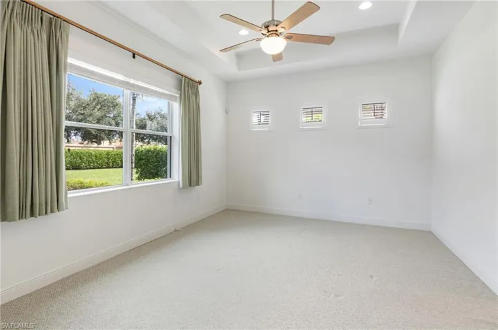 Tray ceiling featuring recessed lighting, multi-speed ceiling fan with integrated light fixture, triple transom windows, and expansive exterior window
