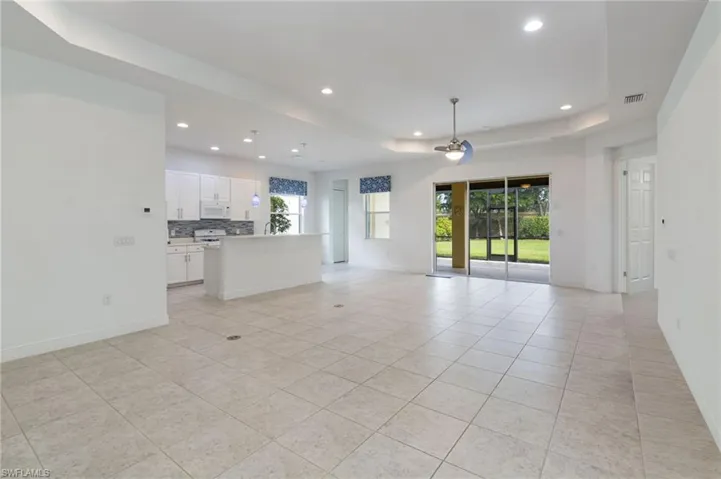 Open-concept interior featuring recessed lighting, tray ceilings, neutral tile flooring, white cabinetry with a breakfast bar, and sliding glass doors