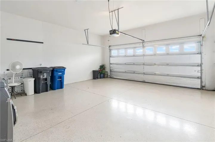 Multi-car garage featuring a sectional door with windows, smooth-finish floor coating, and ceiling-mounted garage door opener