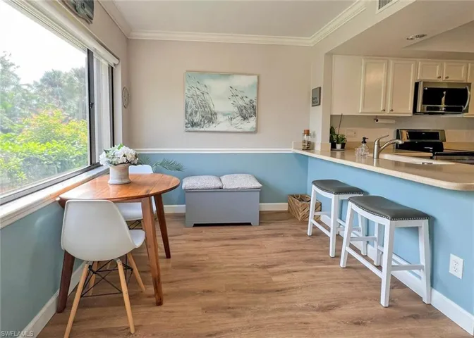 Kitchen featuring appliances with stainless steel finishes, light wood-type flooring, a breakfast bar, white cabinets, and ornamental molding