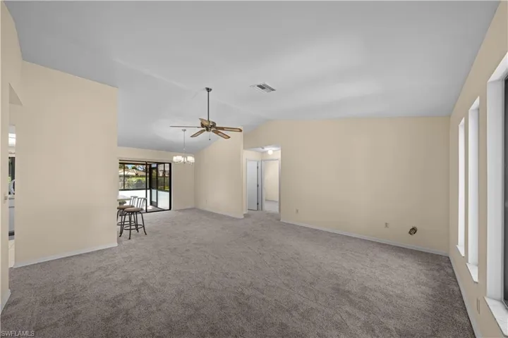 Unfurnished living room featuring light colored carpet, vaulted ceiling, ceiling fan, and a chandelier