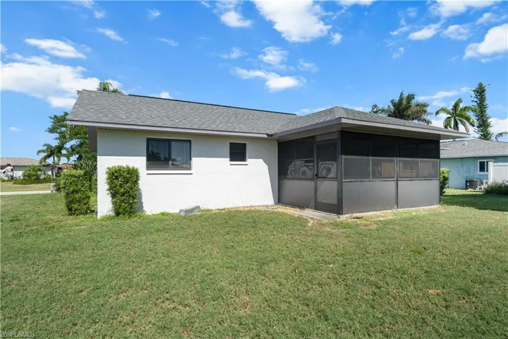 Rear view of house featuring roof with shingles, a sunroom, a lawn, and stucco siding