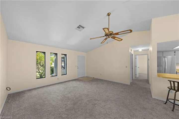 Empty room featuring vaulted ceiling, light carpet, and a ceiling fan