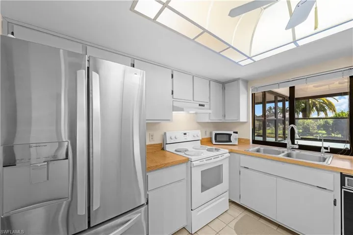 Kitchen with white appliances, light tile patterned floors, white cabinetry, light countertops, and under cabinet range hood