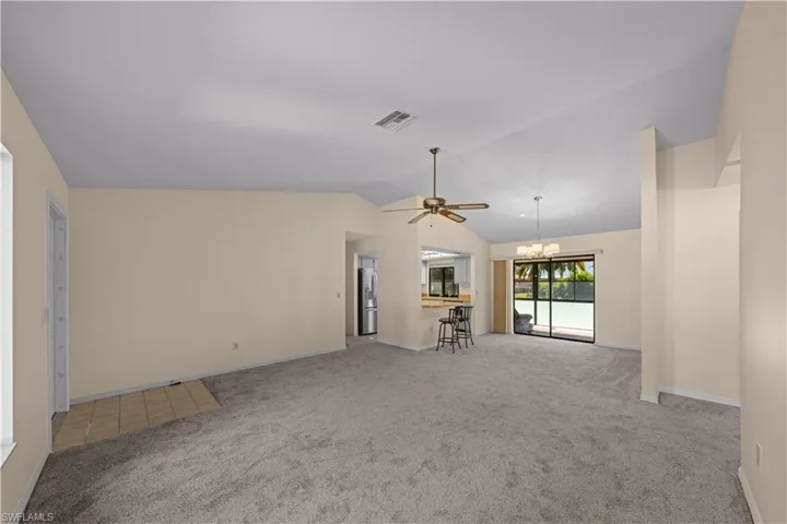 Unfurnished living room featuring a chandelier, light carpet, vaulted ceiling, and ceiling fan