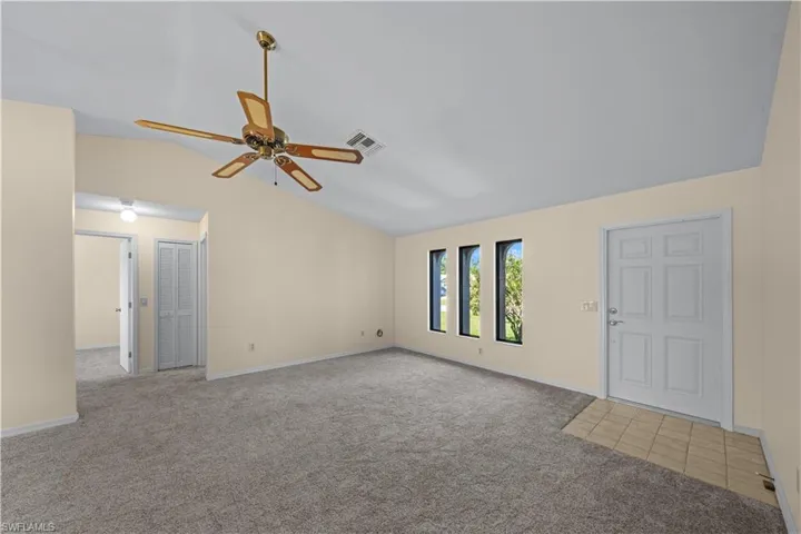 Unfurnished room featuring lofted ceiling, light colored carpet, and a ceiling fan