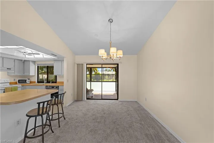 Kitchen with light countertops, light colored carpet, vaulted ceiling, a breakfast bar, and white appliances