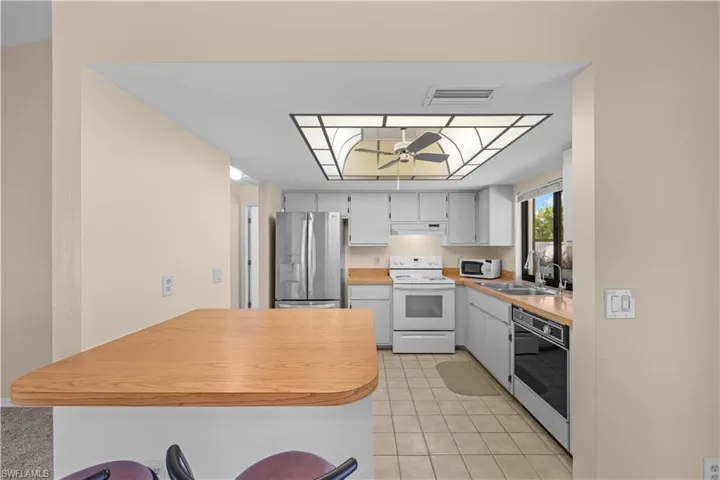 Kitchen featuring a peninsula, light countertops, white appliances, light tile patterned floors, and a breakfast bar